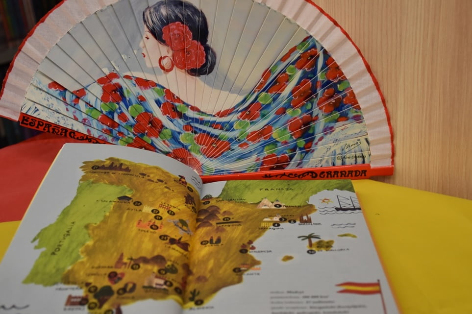 Otwarta książka z mapą Hiszpanii, w tle wachlarz z wizerunkiem kobiety
